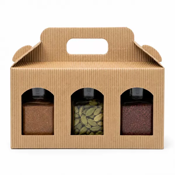 Drei offene Gewürzgläser des Orient Express Sets vor Wellpappe-Geschenkbox: gemahlener Arabischer Pfeffer, ganze grüne Kardamomkapseln und gemahlener Sumach