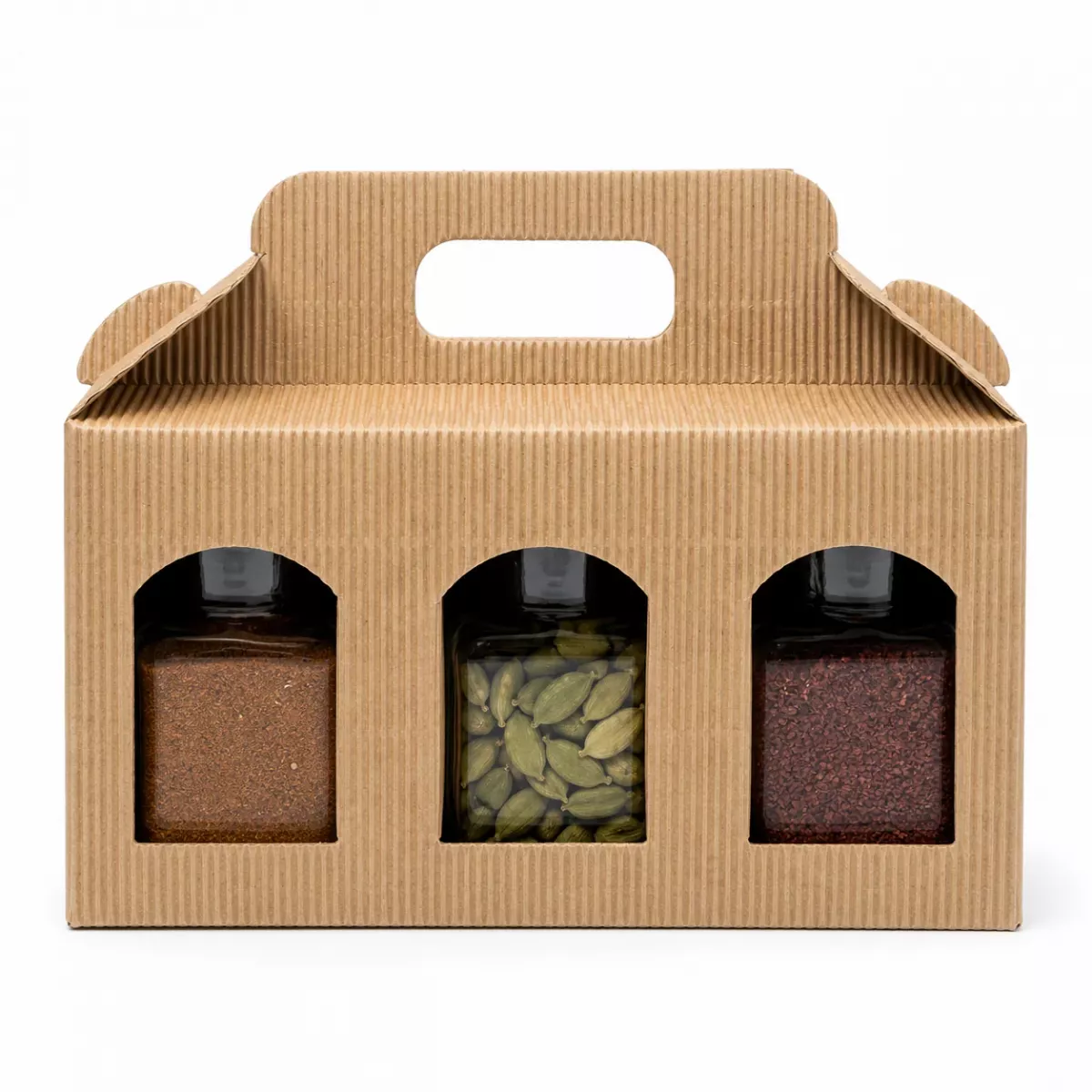 Drei offene Gewürzgläser des Orient Express Sets vor Wellpappe-Geschenkbox: gemahlener Arabischer Pfeffer, ganze grüne Kardamomkapseln und gemahlener Sumach